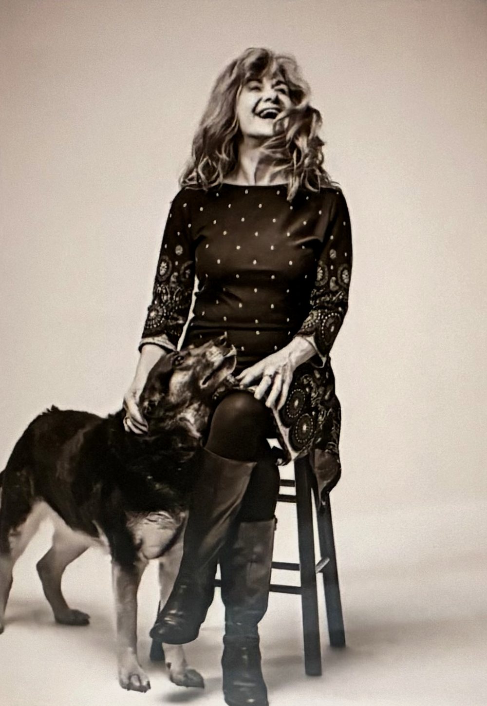 Rebecca L. White laughing, seated on a stool with her German Shepherd