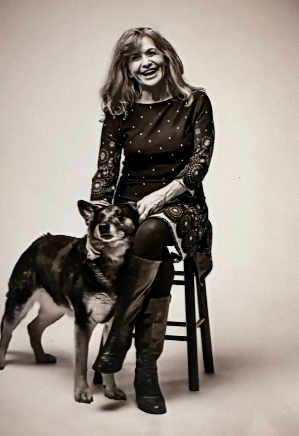 Rebecca L. White smiling at the camera, seated on a stool with her German Shepherd