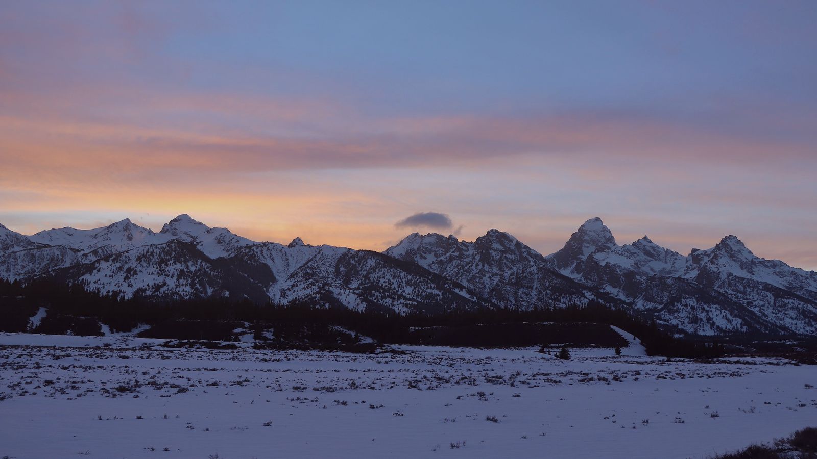 Sunset glowing in soft pink and lavender over the snow-covered Teton Range